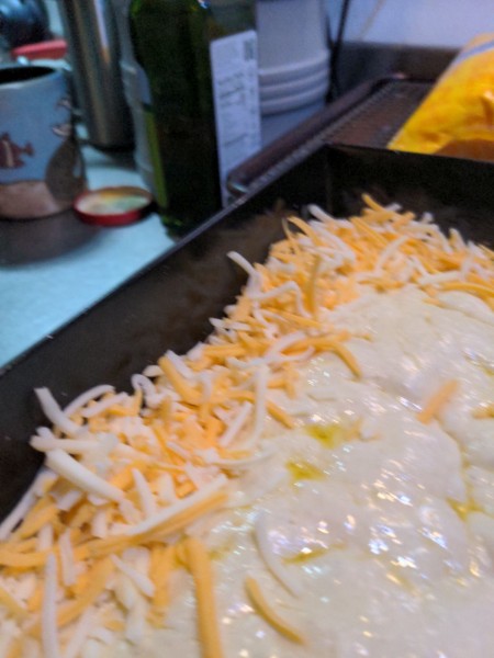 Shredded cheese is piled on the dough much higher than seems correct at the edge of the pan.