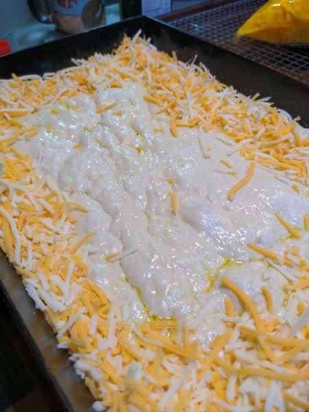 Shredded cheese is piled on the dough all the way around the edge of the pan, coming up close to halfway up the vertical edge of the pan.