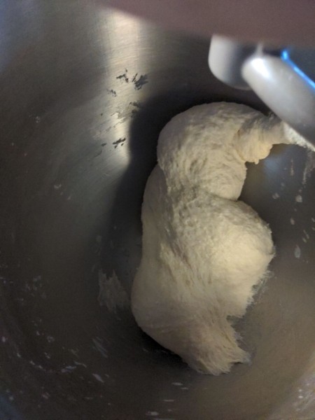 The dough in the bottom of the mixer has formed into a ball, and is now kneading.